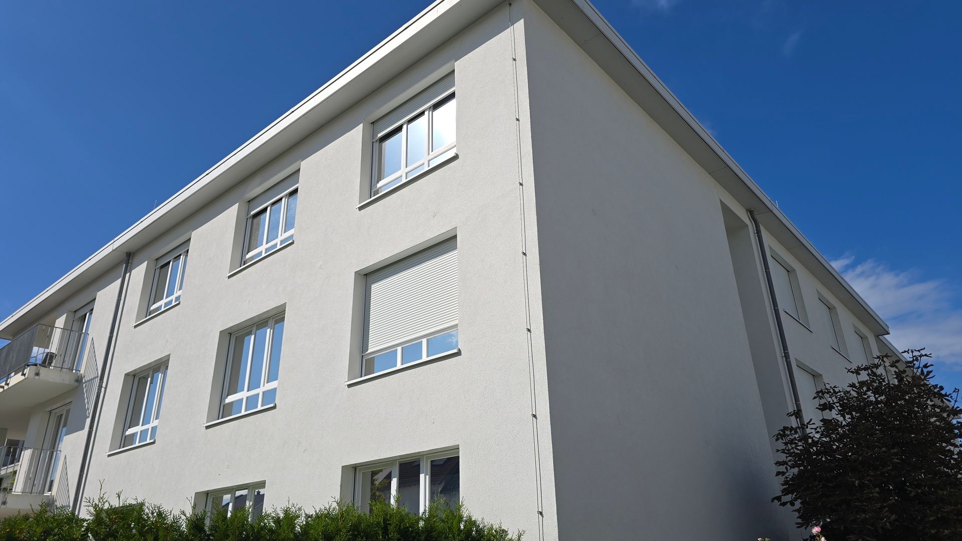 Gereinigtes mehrgeschossiges Wohngebäude mit heller Fassade vor blauem Himmel.