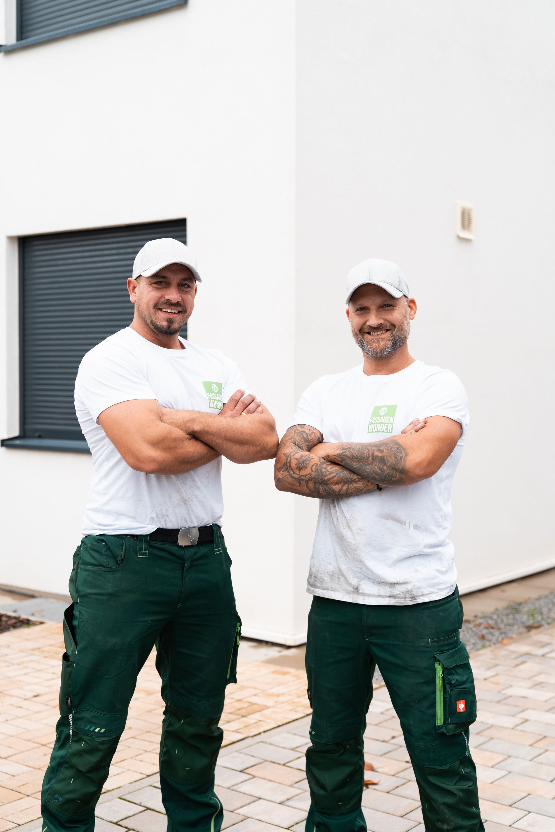 Zwei Mitarbeiter von Fassaden Wunder stehen vor einer frisch gereinigten Hausfassade.
